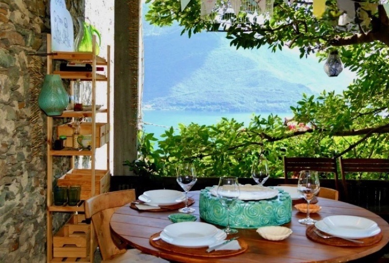 A table set for dinner under the pergola of Casa Artis, the lake glinting through the leaves
