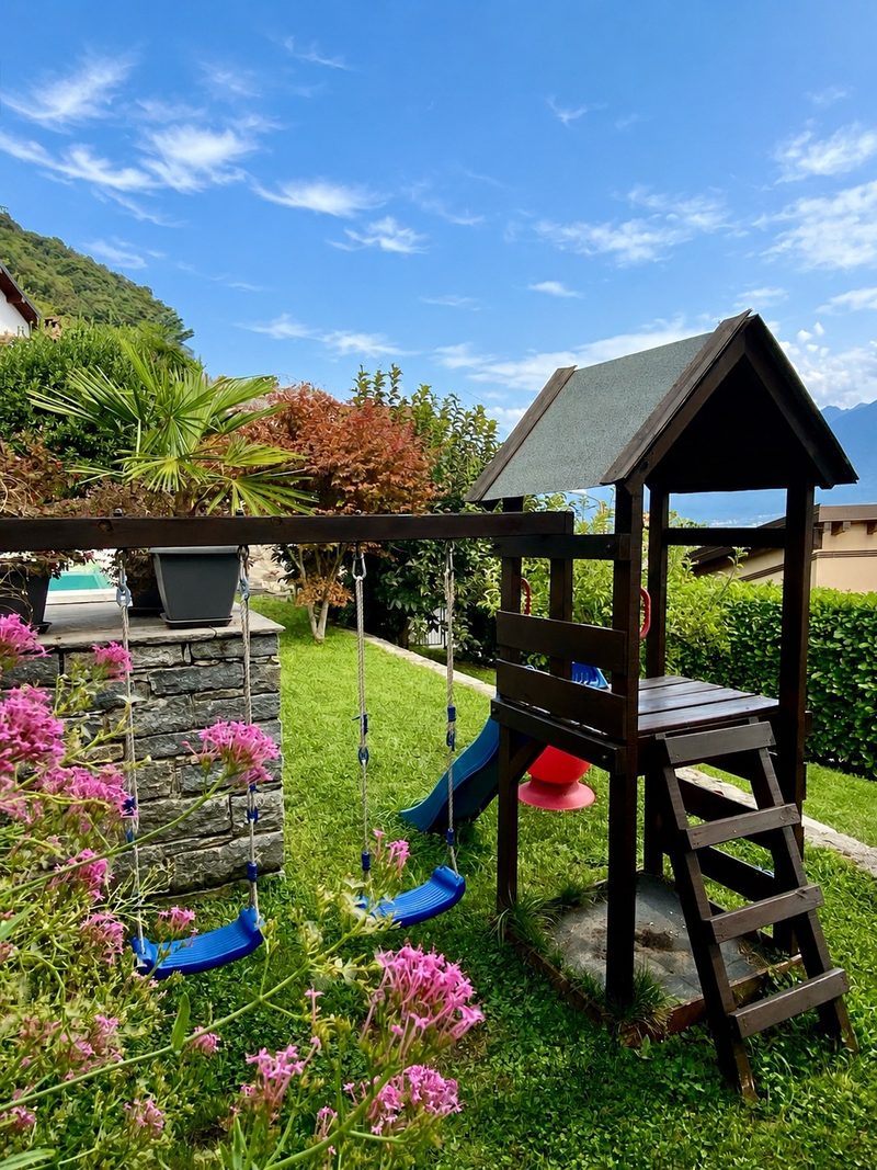 Casa Artis's children's play area with swings and a slide in the garden, among the flowers with the mountains behind