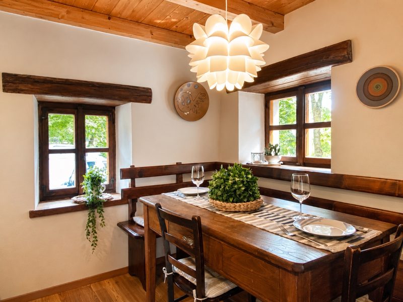 Bucaneve's dining corner with a wooden bench, a flower-shaped pendant lamp and shuttered windows