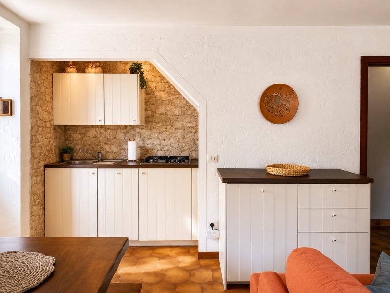 Ciclamino's kitchen units tucked into a niche of golden stone, with the sofa at the edge of the frame