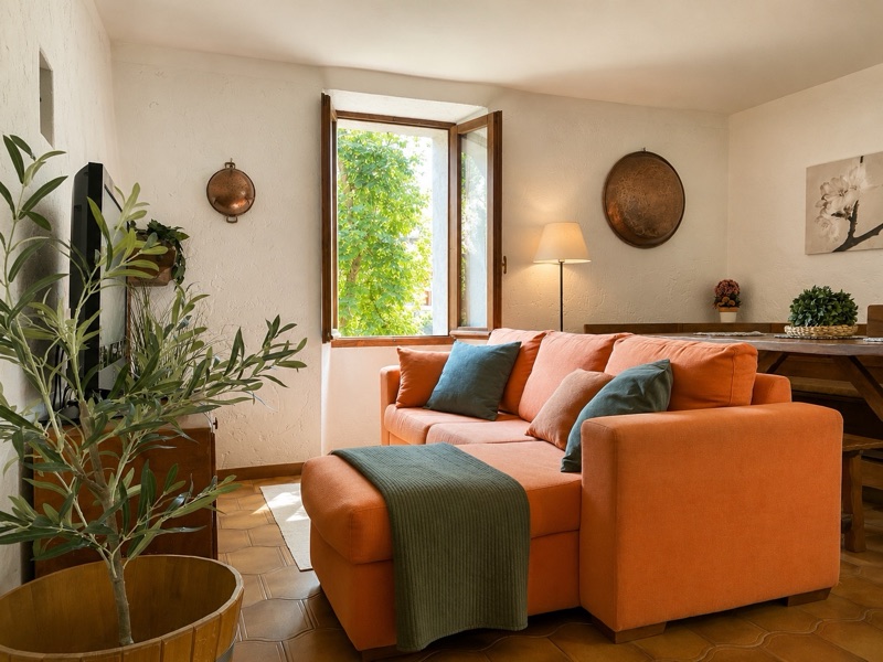 Ciclamino's living room: a terracotta-orange sofa, copper pans on the white walls and sun through the window
