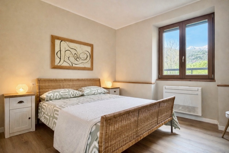 Giardino's bedroom with a rattan bed, patterned linen and a window onto the mountains