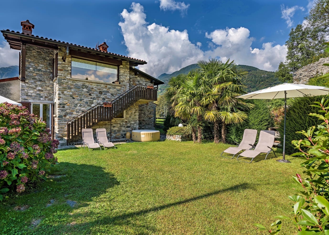 The stone house of Casa Cinzia with its garden, sun loungers, parasols and outdoor jacuzzi