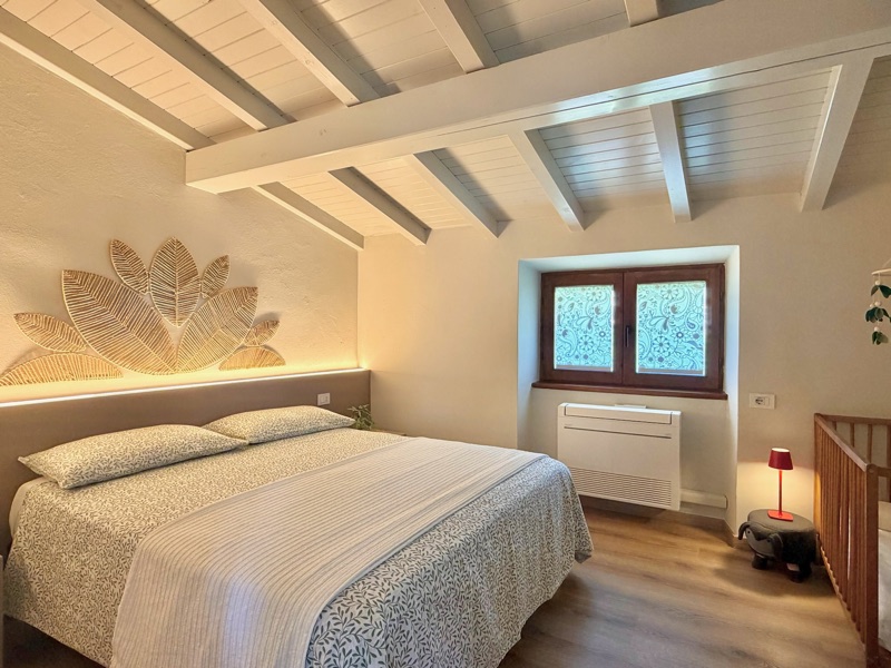 The bedroom of Panorama under white-painted beams, with a woven-leaf headboard