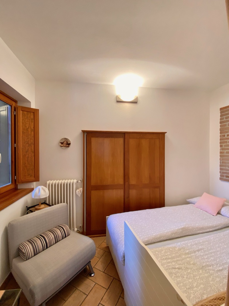 The second bedroom of Dalì with an armchair and warm wooden wardrobe
