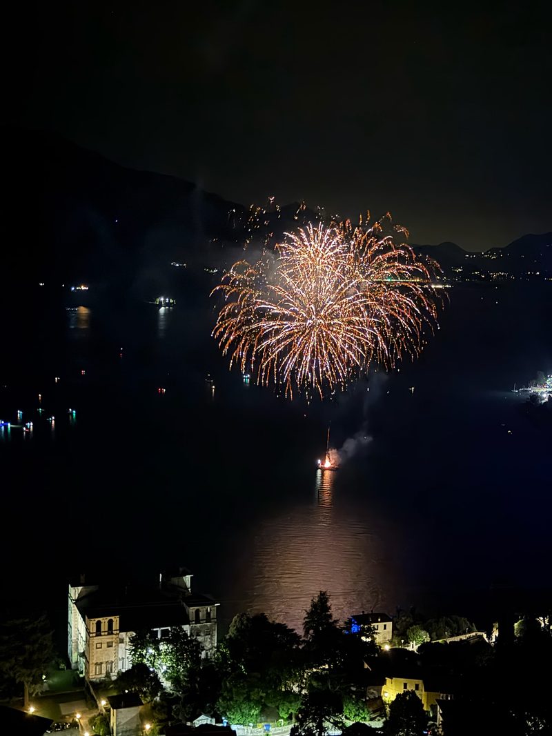 Fireworks over Lake Como seen from above, with the town lights and boats reflected on the water
