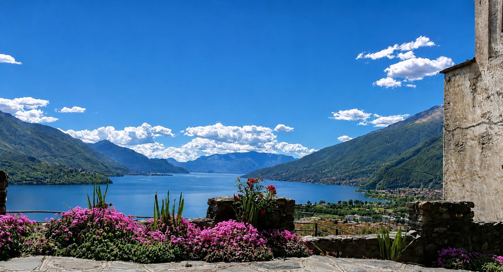 Panoramic view over Lake Como and the surrounding mountains, with flowers in the foreground