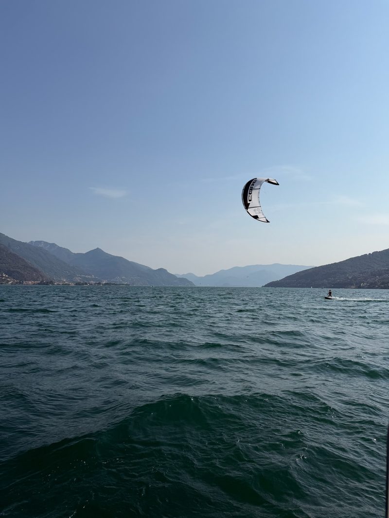 A kitesurfer on Lake Como, the colourful kite riding high above the water with mountains all around