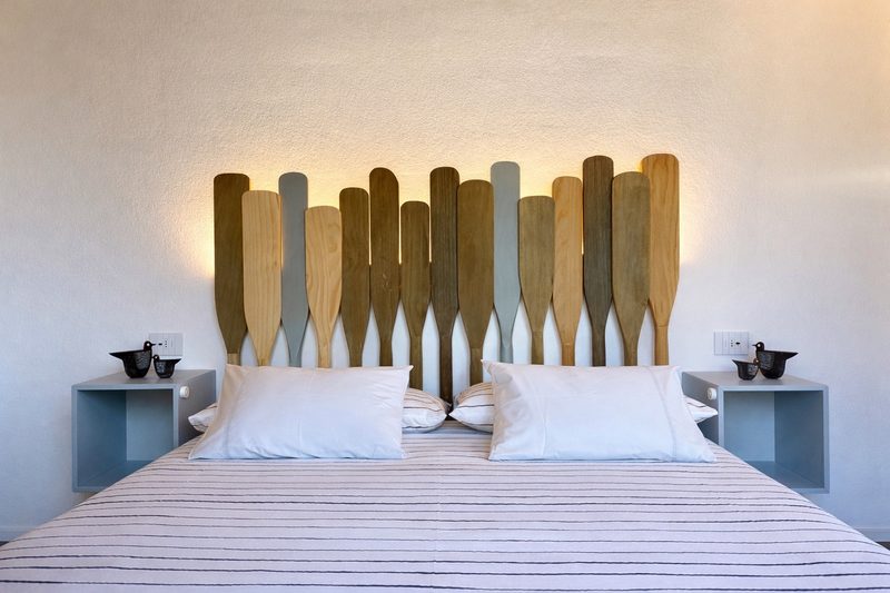 A bedroom whose headboard is made of weathered wooden oars, softly backlit