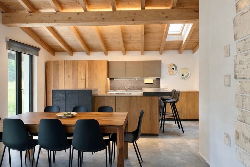 The open kitchen and long wooden dining table of Villa Larius under exposed timber beams and a skylight