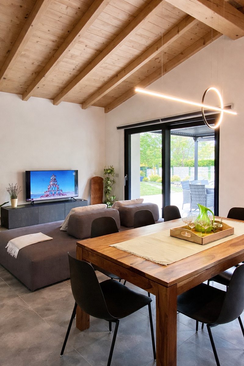 Villa Larius' living room with grey sofas, a ring light fitting and glass doors onto the pergola