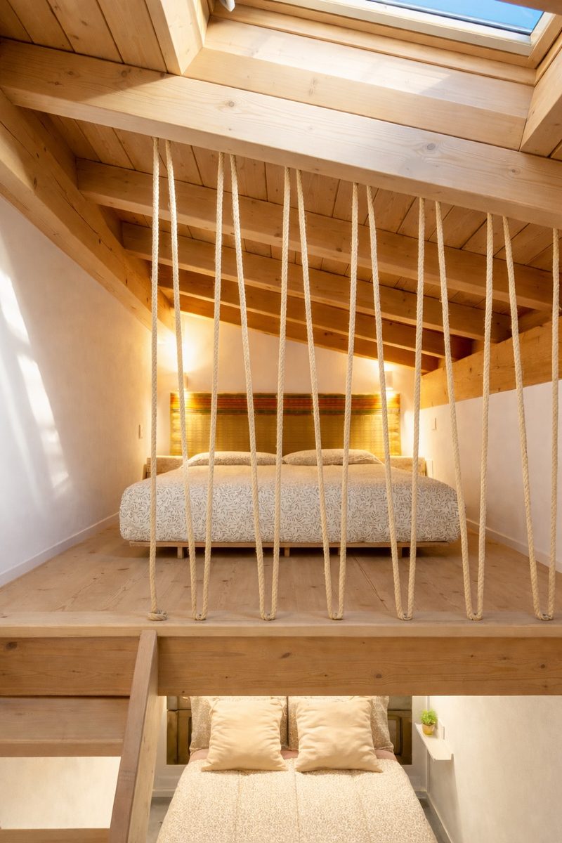 The mezzanine sleeping loft under a skylight, screened by slender wooden spindles