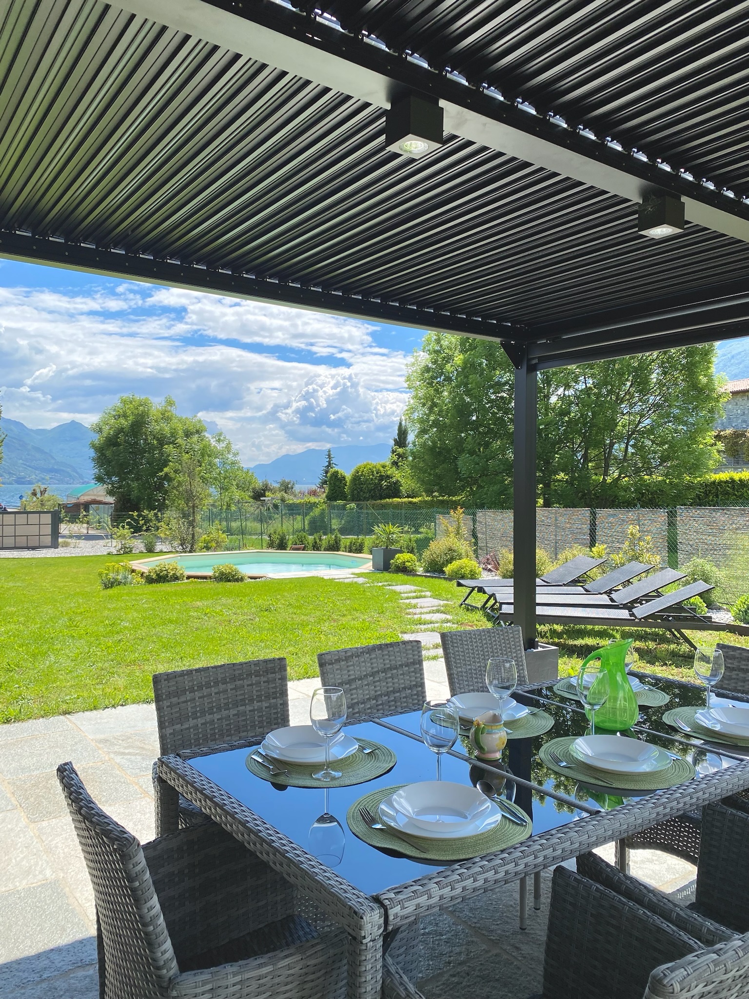 The table set for lunch under Villa Larius' louvred pergola, with the pool and mountains beyond