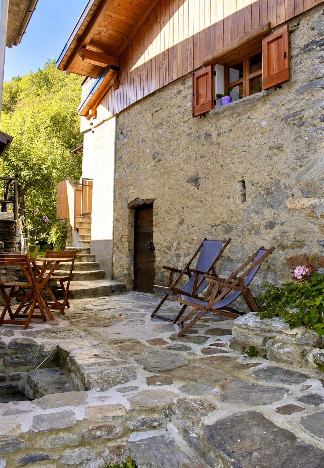 The outdoor space shared between Bucaneve and Ciclamino, with the wooden balcony, a table laid outside and the parasol in the garden