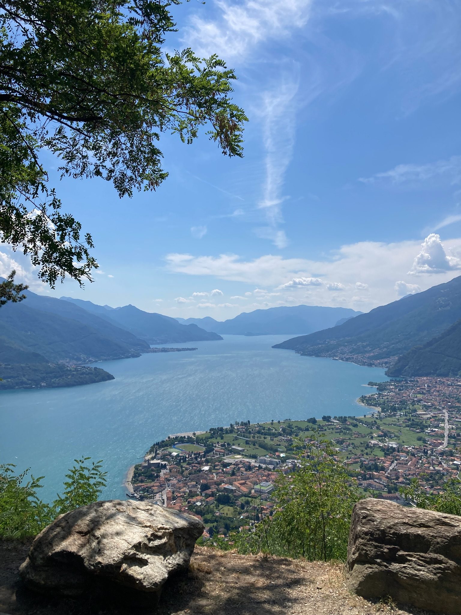 The view over Lake Como from Naro, framed by tree branches, with the mountains and the town in the distance