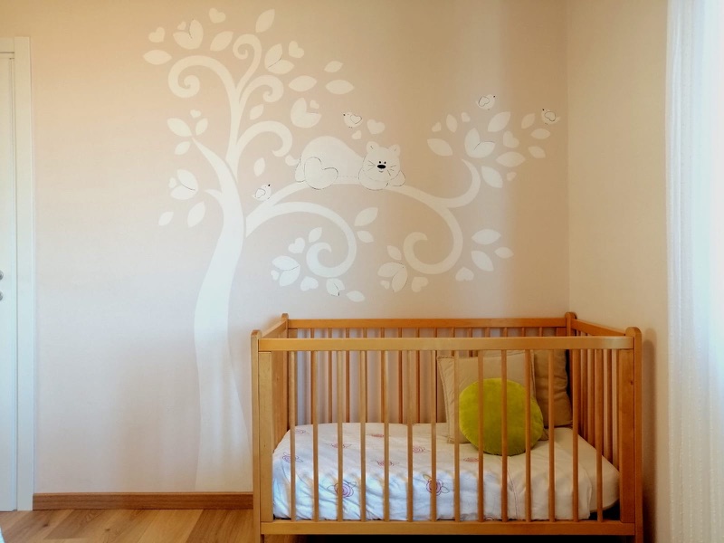 A cot beneath a hand-painted tree in Picasso's nursery corner